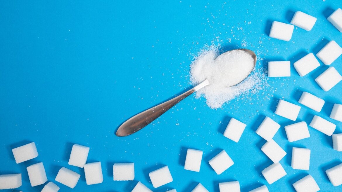 Cucchiaio con dolcificante in polvere e zollette di zucchero su sfondo azzurro, simbolo degli edulcoranti come alternativa allo zucchero