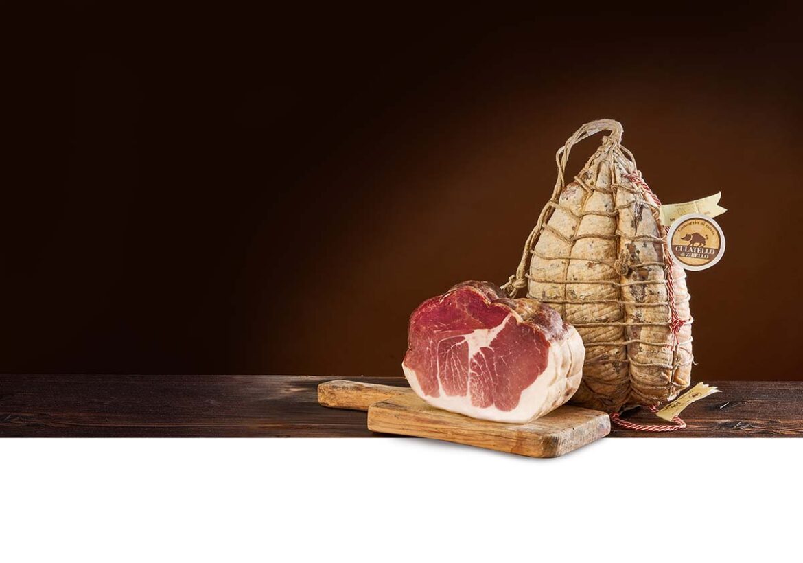 Un Culatello di Zibello DOP intero legato con lo spago e un pezzo tagliato su un tagliere di legno.