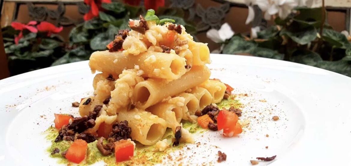 Mezzi ziti al baccalà e olive taggiasche impiattati su letto di pesto